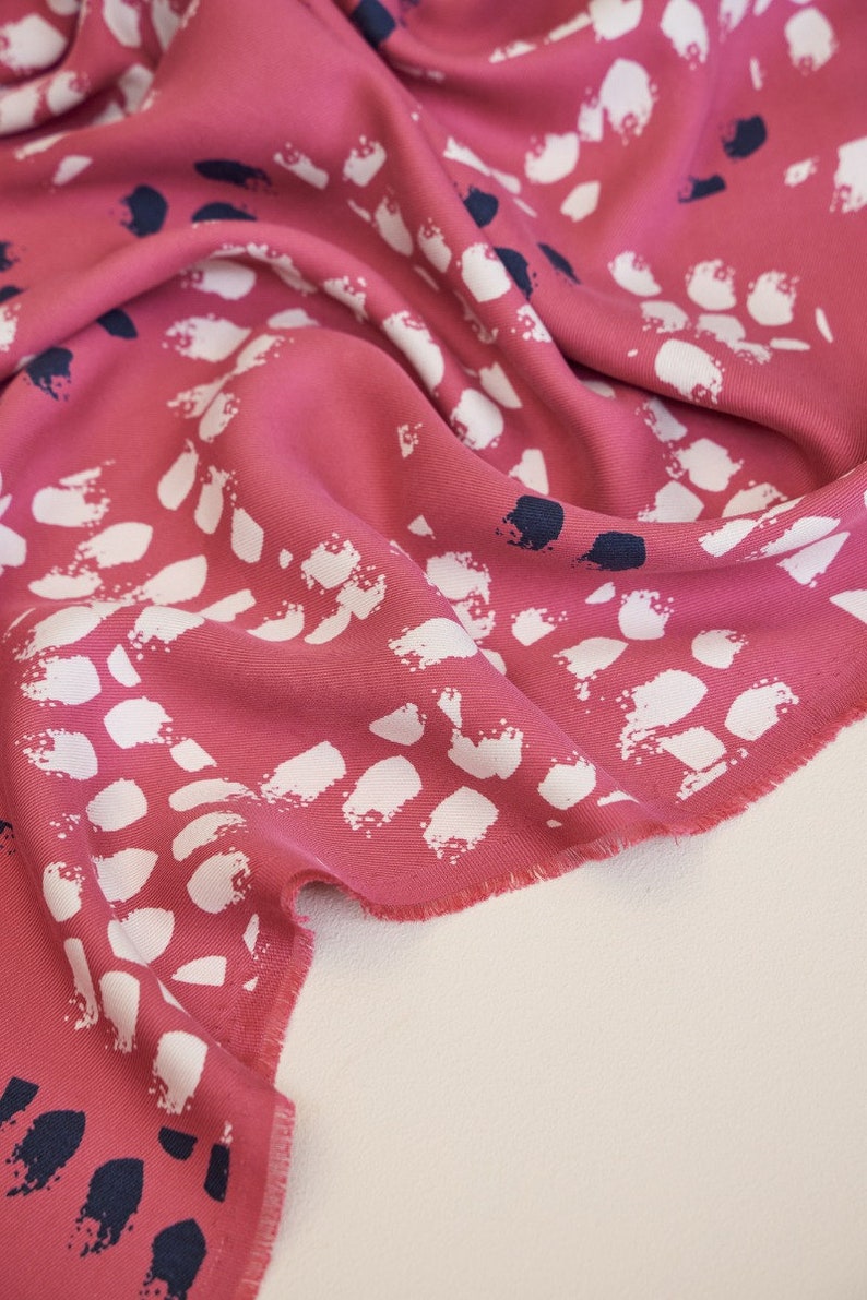 Pu&ograve; includere: Tessuto rosa con una stampa astratta bianca e blu navy. Il tessuto &egrave; piegato e i bordi sono sfilacciati.