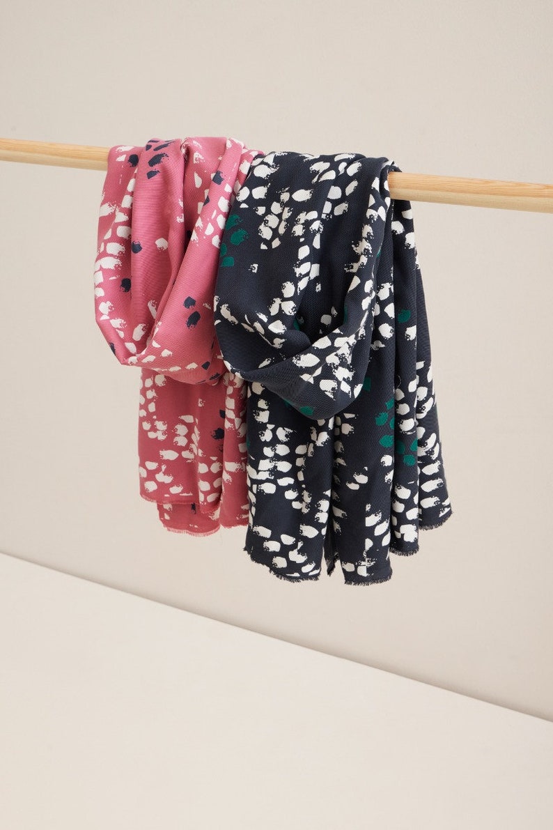 Pu&ograve; includere: Due sciarpe con un motivo astratto bianco e nero. Una sciarpa &egrave; rosa e l'altra &egrave; blu scuro.