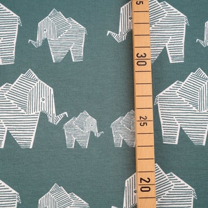 Könnte beinhalten: Tealfarbener Stoff mit einem weißen geometrischen Elefantenmuster. Der Stoff wird mit einem Lineal in Zentimetern gemessen.