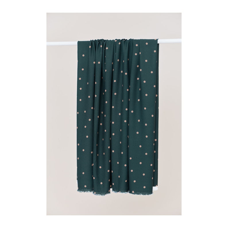 May include: A dark green fabric with a white polka dot pattern. The fabric is hanging from a white rod.