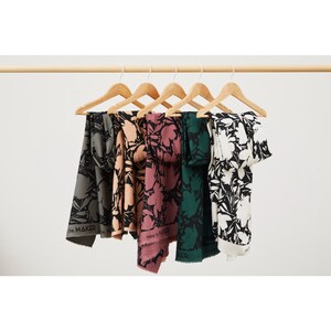 Puede incluir: Cinco pa&ntilde;uelos de tela con estampado floral en blanco y negro. Los pa&ntilde;uelos est&aacute;n colgados de perchas de madera. Los pa&ntilde;uelos son de diferentes colores: verde, rosa, melocot&oacute;n y gris.