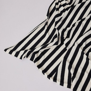 Może przedstawiać: Czarno-biała tkanina w paski, prawdopodobnie odzież lub tkanina, jest ułożona na białym tle. Tkanina ma odważne, pionowe paski, tworząc uderzający kontrast wizualny. Materiał wydaje się miękki i płynny.