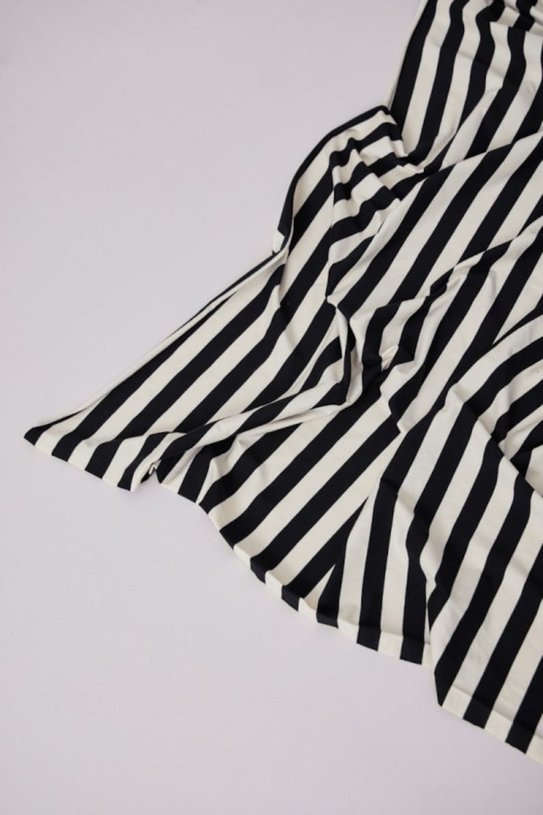 Może przedstawiać: Czarno-biała tkanina w paski, prawdopodobnie odzież lub tkanina, jest ułożona na białym tle. Tkanina ma odważne, pionowe paski, tworząc uderzający kontrast wizualny. Materiał wydaje się miękki i płynny.