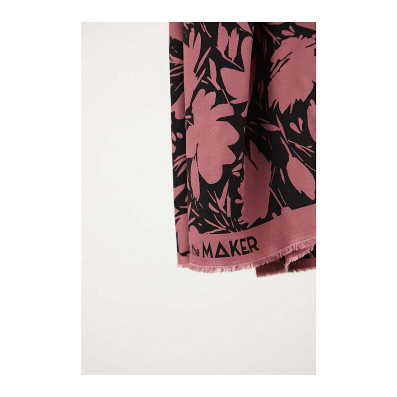 Puede incluir: Una tela rosa con estampado floral negro. La tela tiene un borde deshilachado y el texto "the MAKER" impreso en la parte inferior.