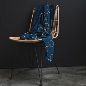 Könnte beinhalten: Ein dunkelblauer Stoff mit goldenen Kreisen und dem Text "mind the MAKER", der über einen Korbstuhl mit schwarzen Metallbeinen gelegt ist.