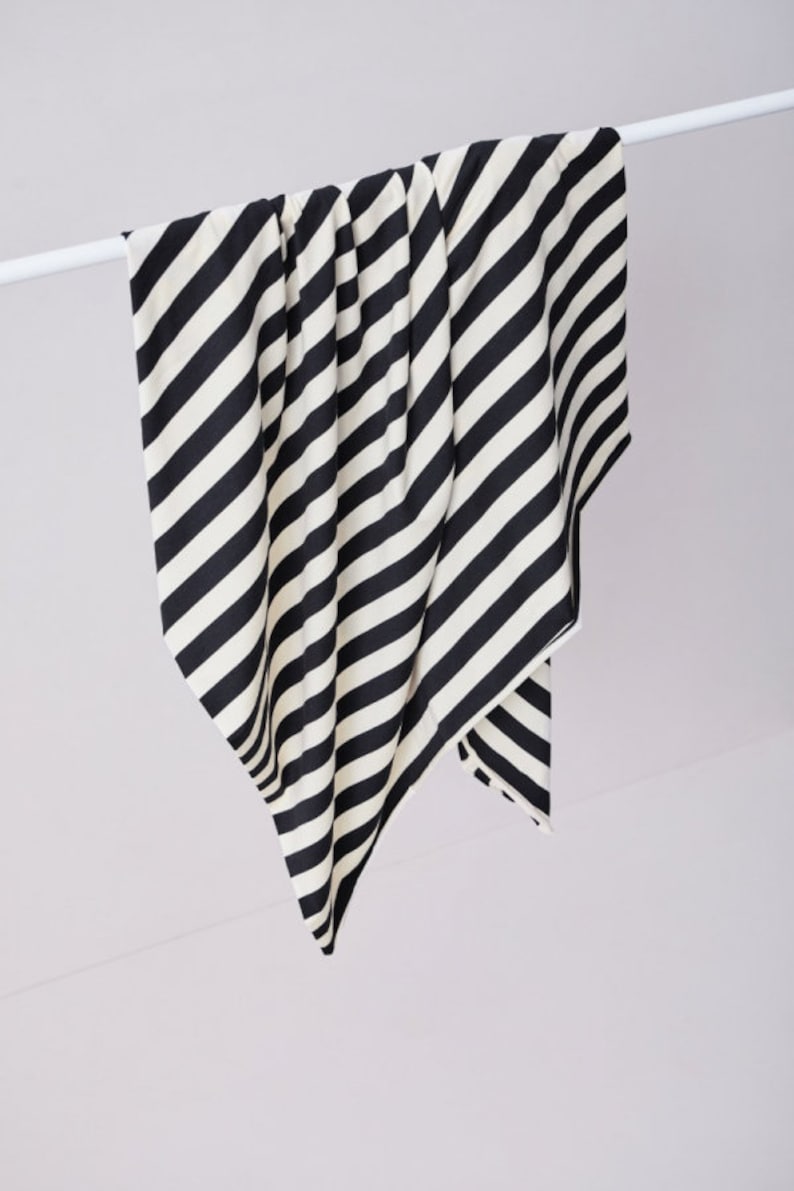 Może przedstawiać: Czarno-biała szalik lub szal w paski jest zawieszony na białym pręcie. Tkanina ma odważne, ukośne paski. Szalik jest wykonany z miękkiego materiału i wisi na gładkim, białym tle.