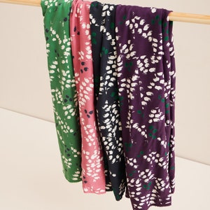 Pu&ograve; includere: Quattro campioni di tessuto con un motivo astratto bianco su sfondo verde, rosa, blu navy e viola. Il tessuto &egrave; appeso a un'asta di legno.