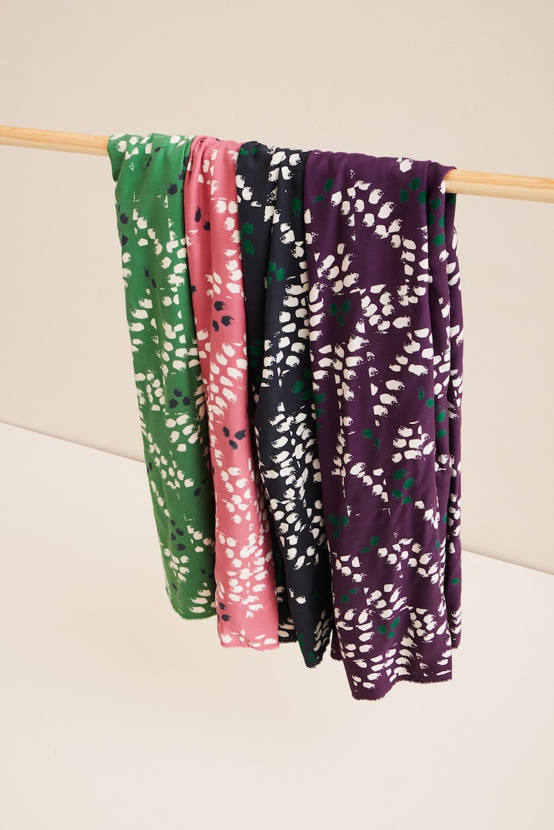 Pu&ograve; includere: Quattro campioni di tessuto con un motivo astratto bianco su sfondo verde, rosa, blu navy e viola. Il tessuto &egrave; appeso a un'asta di legno.