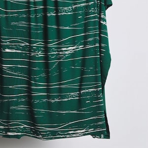 Può includere: Tessuto verde con un motivo astratto bianco di linee e onde. Il tessuto ha una texture morbida e fluida.