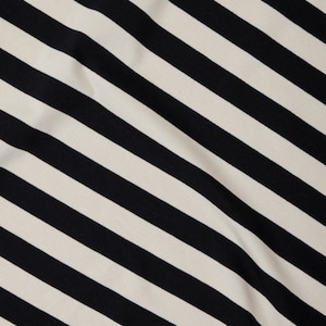 Może przedstawiać: Zbliżenie tkaniny z ukośnym wzorem w czarno-białe paski. Paski są r&oacute;wnomiernie rozmieszczone i przebiegają przez tkaninę. Tkanina wydaje się miękka i lekko teksturowana.