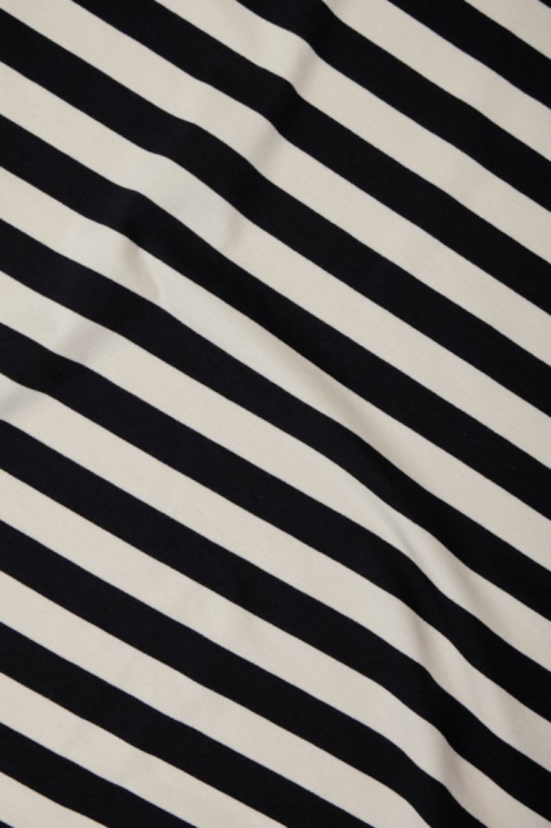 Może przedstawiać: Zbliżenie tkaniny z ukośnym wzorem w czarno-białe paski. Paski są r&oacute;wnomiernie rozmieszczone i przebiegają przez tkaninę. Tkanina wydaje się miękka i lekko teksturowana.