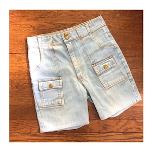 Pode incluir: Calções de ganga azul claro com dois bolsos cargo frontais e dois bolsos traseiros. Os calções têm fecho de botão e zíper e são feitos de ganga clara. Um estilo clássico.