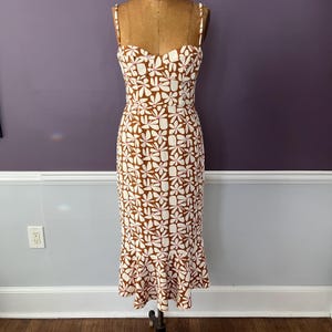 May include: A brown and white floral print dress with a sweetheart neckline and spaghetti straps. The dress has a fitted bodice and a flared skirt, displayed on a mannequin. The floral pattern is composed of white flowers with pink accents.