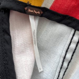 May include: Close-up of a garment tag with the brand name "Free People" in a dark brown color. The tag is attached to a black fabric. The tag reads "MADE IN CHINA / FABRIQUE EN CHINE".