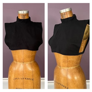 May include: A black turtleneck collar, displayed on a vintage wooden dress form. The collar is a solid black color and has a high neckline. The dress form has the words "COLLAPSIBLE MODEL FORM" printed on it.