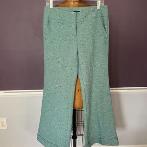 May include: Mint green trousers featuring a textured tweed-like fabric with small black and white flecks. These pants have a wide-leg silhouette, a front zipper closure, side pockets, and a cuffed hemline, displayed on a dress form.