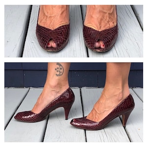 May include: Burgundy peep-toe heels with a snakeskin pattern. The shoes have a pointed toe and a stiletto heel. The image shows the shoes from multiple angles, highlighting the texture and design.