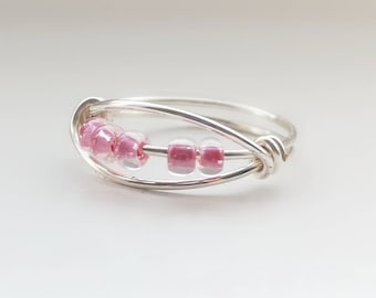 May include: A silver ring with a delicate wire design and pink beads.