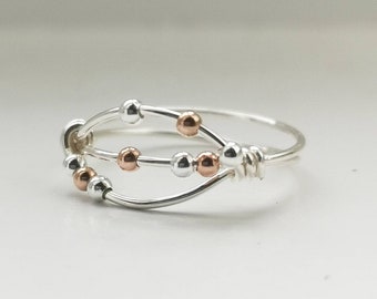 May include: A silver ring with a delicate design featuring two intertwined bands and small silver and rose gold beads.