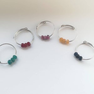 May include: Five silver rings, each with three gemstone beads. The rings are arranged in a row, with the beads in the following colours: green, red, pink, yellow, and black.