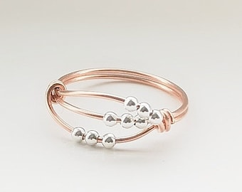 May include: A delicate rose gold ring with a double band design featuring a cluster of silver beads.