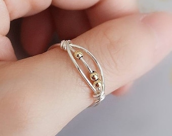 May include: A silver ring with three gold beads on a finger.