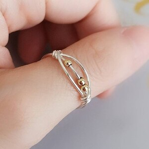 May include: A silver ring with three gold beads on a finger.