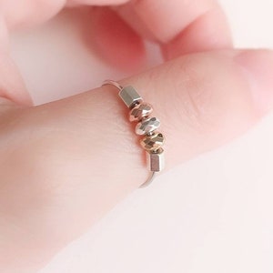 May include: A silver ring with a row of small, round beads in silver, gold, and rose gold.