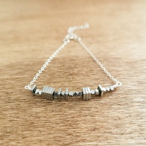 May include: A silver chain bracelet with a row of small, silver, geometric-shaped beads.