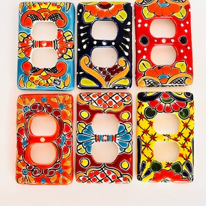 May include: Six rectangular ceramic electrical outlet covers featuring hand-painted floral and geometric patterns in vibrant colors including blue, red, orange, yellow, and black. Each cover has two circular cutouts for standard duplex outlets.