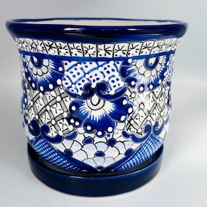May include: A ceramic planter with a matching saucer, featuring a vibrant blue and white hand-painted pattern. The design includes intricate floral motifs, geometric lattice work, and scalloped borders, with a solid dark blue rim and base.