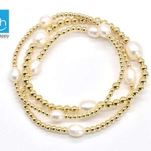 May include: A gold beaded bracelet with white pearls. The bracelet is made of three strands of gold beads and has a total of seven pearls.