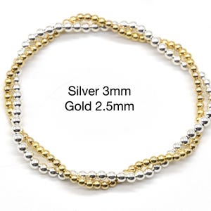 May include: Two beaded bracelets, one silver with 3mm beads and one gold with 2.5mm beads. The bracelets are intertwined, showcasing the contrast between the metallic colors. The text "Silver 3mm Gold 2.5mm" is visible.