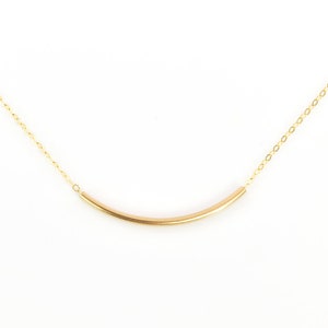 May include: A delicate gold-colored necklace with a curved bar pendant. The pendant is suspended from a fine chain. The jewelry is displayed against a white background, highlighting the necklace's simple elegance.