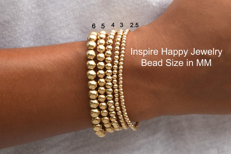 May include: Gold beaded bracelets in various sizes are displayed on a wrist. The beads range from 2.5mm to 6mm in diameter. The text "Inspire Happy Jewelry Bead Size in MM" is visible.