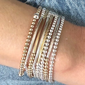 May include: A stack of silver and gold beaded bracelets on a person's wrist. The bracelets are layered and create a stylish and modern look.