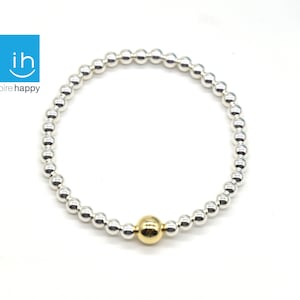 May include: Silver beaded bracelet with a single gold bead. The bracelet is made of small, round silver beads and a larger, gold-colored bead. The bracelet is displayed on a white background. The logo "inspire happy" is in the top left corner.