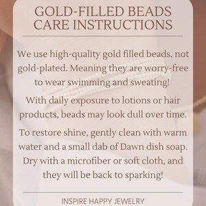 May include: A beige card with the text "GOLD-FILLED BEADS CARE INSTRUCTIONS" and care tips for gold-filled beads. The card advises cleaning with warm water and soap to restore shine. The brand name "INSPIRE HAPPY JEWELRY" is at the bottom.