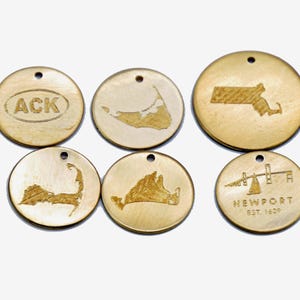May include: Six gold-colored metal charms with different designs. The charms feature the text "ACK", "NEWPORT EST. 1639", and outlines of the states of Massachusetts and Rhode Island, as well as the islands of Martha's Vineyard and Nantucket.