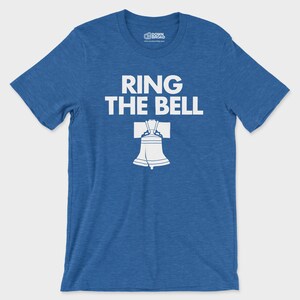 K&ouml;nnte beinhalten: Ein meliertes k&ouml;nigsblaues Kurzarm-T-Shirt mit dem wei&szlig;en Schriftzug "RING THE BELL" &uuml;ber einer wei&szlig;en grafischen Abbildung der Liberty Bell. Das T-Shirt hat einen Rundhalsausschnitt und ein Markenetikett auf der Innenseite des Kragens.