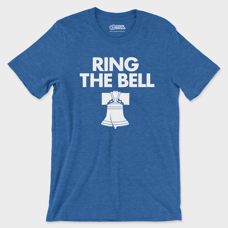 K&ouml;nnte beinhalten: Ein meliertes k&ouml;nigsblaues Kurzarm-T-Shirt mit dem wei&szlig;en Schriftzug "RING THE BELL" &uuml;ber einer wei&szlig;en grafischen Abbildung der Liberty Bell. Das T-Shirt hat einen Rundhalsausschnitt und ein Markenetikett auf der Innenseite des Kragens.