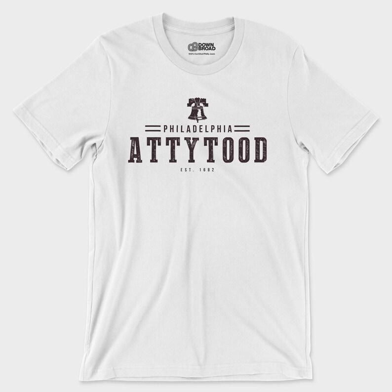 Puede incluir: Una camiseta blanca de manga corta con un gr&aacute;fico oscuro en el pecho. El dise&ntilde;o incluye un icono de la Liberty Bell sobre el texto PHILADELPHIA, la palabra ATTYTOOD en letras may&uacute;sculas grandes y el texto EST. 1682 debajo.