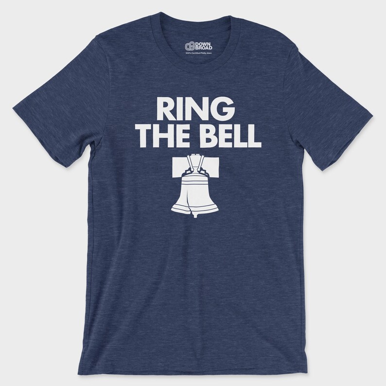 K&ouml;nnte beinhalten: Ein kurz&auml;rmeliges T-Shirt in meliertem Marineblau mit dem wei&szlig;en Schriftzug "RING THE BELL" &uuml;ber einer Grafik der Liberty Bell. Das T-Shirt hat einen Rundhalsausschnitt und ein Markenlogo im inneren Kragenbereich.