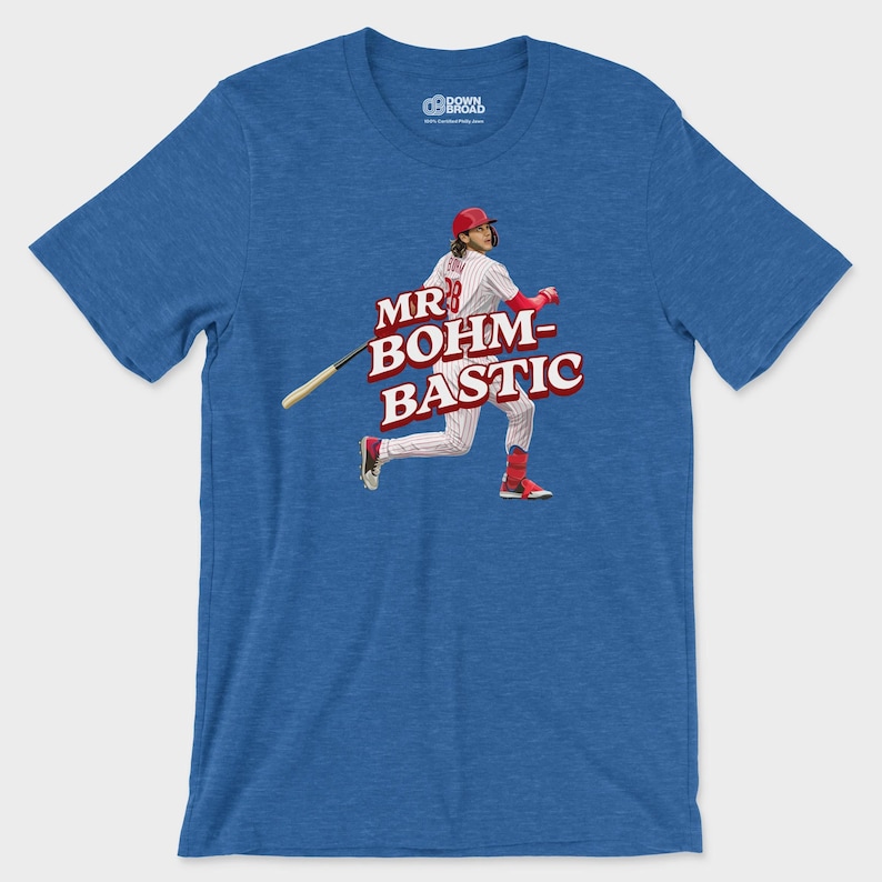 May include: A heather blue short-sleeve t-shirt featuring a graphic of a baseball player in a white pinstripe uniform with a red helmet and bat. The text MR BOHM-BASTIC is printed in large red letters across the center of the chest area.