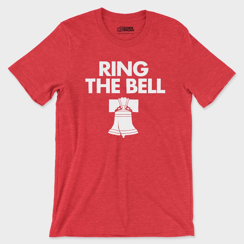 K&ouml;nnte beinhalten: Ein rotes Kurzarm-T-Shirt mit melierter Textur. Auf der Vorderseite befindet sich der wei&szlig;e Schriftzug "RING THE BELL" &uuml;ber einer wei&szlig;en grafischen Abbildung der Liberty Bell. Das innere Nackenetikett zeigt den Text "DOWN BROAD".