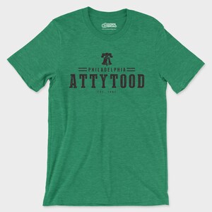 Puede incluir: Una camiseta de manga corta en color verde jaspeado con un gr&aacute;fico negro en el pecho. El dise&ntilde;o incluye un icono de la Liberty Bell sobre el texto PHILADELPHIA ATTYTOOD y EST 1892. La camiseta tiene cuello redondo y un acabado de tela texturizada.