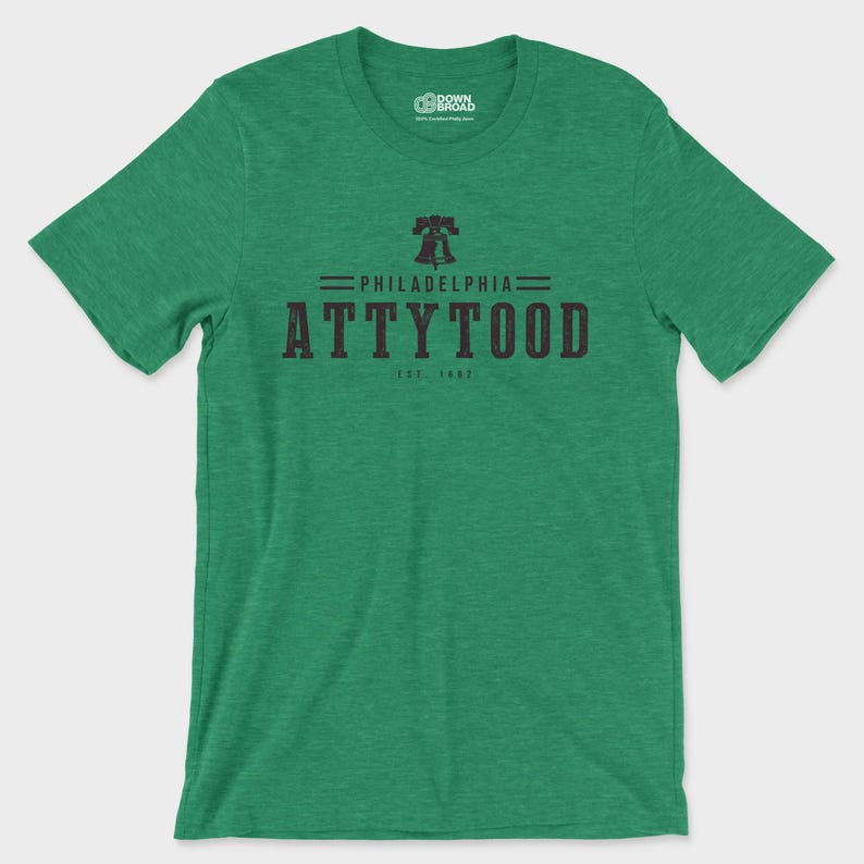 Puede incluir: Una camiseta de manga corta en color verde jaspeado con un gr&aacute;fico negro en el pecho. El dise&ntilde;o incluye un icono de la Liberty Bell sobre el texto PHILADELPHIA ATTYTOOD y EST 1892. La camiseta tiene cuello redondo y un acabado de tela texturizada.