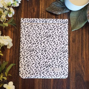 May include: A white e-reader case with a black and white musical note pattern. The case has a small logo that says "Book Nook".