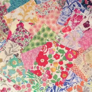 May include: A collection of colorful fabric squares with floral and patterned designs. The fabrics feature a variety of colors, including pink, red, blue, green, and yellow. The arrangement of the squares creates a visually appealing patchwork effect, suitable for crafting projects.