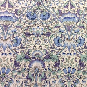 May include: A white fabric with a repeating pattern of blue and purple flowers and leaves. The pattern is intricate and detailed, with a vintage aesthetic.